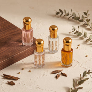 Four Oud Library perfume oil roll ons with gold caps on a cream surface with a wooden corner and eucalyptus