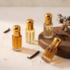 Four Oud Library perfume oil roll ons in gold topped bottles with dried vanilla pods on a cream surface